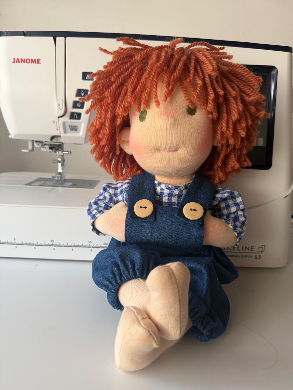 El muñeco del overol, ya terminado, sentado delante de la máquina de coser.